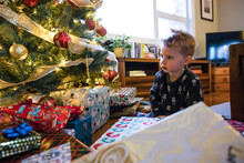 Cute Curious Toddler Boy Looking At Lit Christmas Tree And Gifts