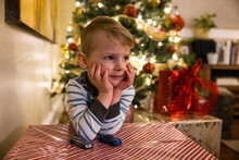 Cute Toddler Boy Leaning On Gift By Lit Christmas Tree