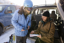 Snowboarding Friends With Map At SUV In Parking Lot