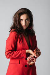 Wall Mural - brunette woman in trendy suit holding red pomegranate isolated on grey.