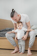 © Anastasiya Reiter - Smiling father dressing his baby son sitting on bed. White background.