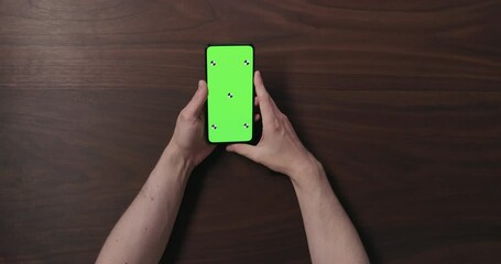 Sticker - Top view slow motion man hand hold smartphone with green screen over black walnut wood table