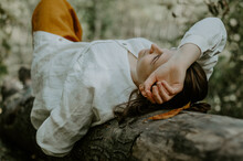Woman In White Linen Shirt Relaxed On A Fallen Tree Trunk, Looking Up
