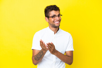 Wall Mural - Young handsome Brazilian man isolated on yellow background applauding after presentation in a conference