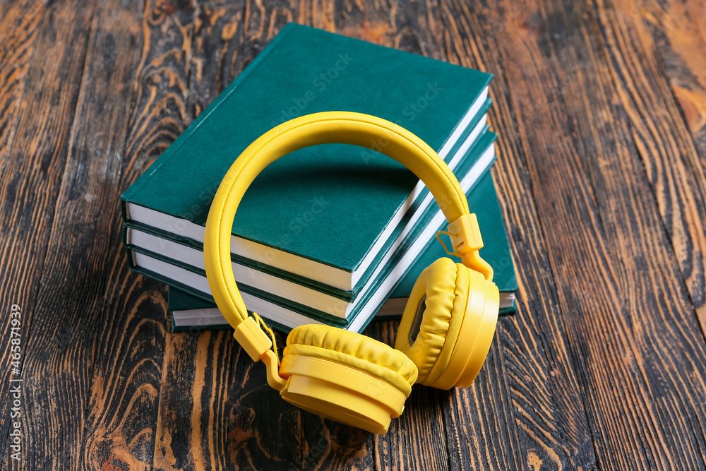 Modern headphones and books on wooden background