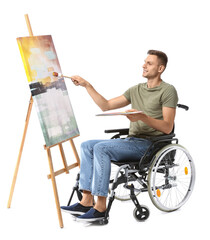 Young male artist in wheelchair painting picture against white background