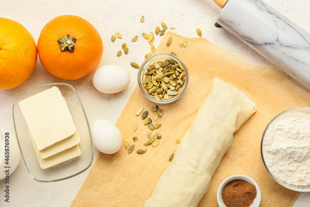 Raw dough and ingredients for preparing pumpkin strudel on light background
