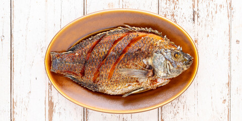 tasty large fried nile tilapia fish in oval ceramic plate on white wooden texture background with copy space for text, top table view, flat lay, 2 x 1 ratio