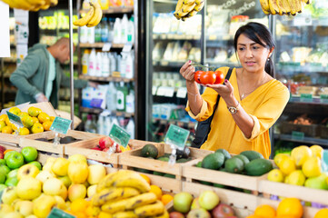 Woman shopper chooses ripe tomatoes at grocery supermarket