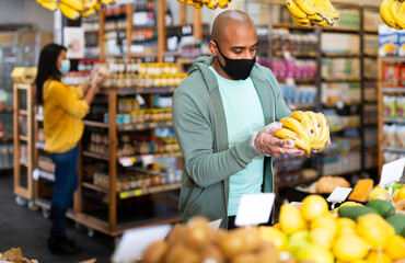 Man in protective mask picks ripe bananas at grocery supermarket