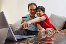 Father And Son Together Shopping Online Through Laptop Using Credit Card