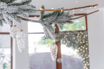 Wall Mural - Elegant snow-covered branch of Christmas tree with wooden drift hangs under the white ceiling.