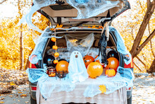 Cute Apricot Poodle Dog In Ghost Costume Sits In Trunk Of Car Decorated For Halloween With Cobwebs, Orange Balloons, Pumpkins And Sweets, The Outdoor Creative Activity Concept In Autumn In October