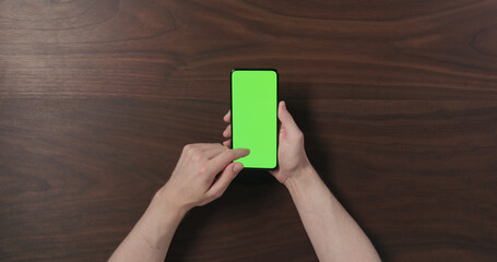 Sticker - Top view man hands hold smartphone with green screen over black walnut wood table