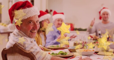 Wall Mural - Yellow star icons falling against caucasian senior man smiling while having dinner during christmas