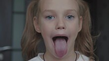 Child Girl Opens Her Mouth Wide. Child Shows Her Teeth And Mouth To Dentist. Mouth Is Wide Open, Tongue Is Stuck Out As Far As Possible, With Clear View Of Tongue And Soft Palate
