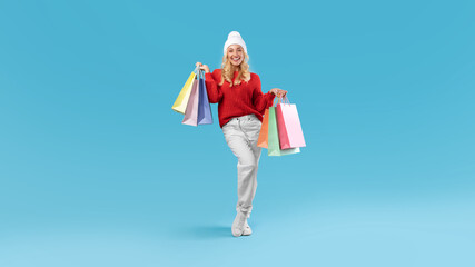 Smiling woman in winter hat holding shopping bags at studio