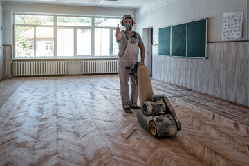 Wall Mural - man sands the parquet in the classroom and shows a thumbs up