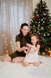 © Maria - a mother with a small daughter playing with a hamster at christmas tree. give a pet to a child for the new year. happy childhood.