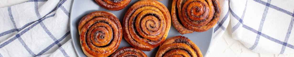 Wall Mural - banner of baked cinnamon buns on grey plate on light background with checkered napkin