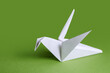 © OlPhoto - White paper crane on a green background close-up. Crafts from paper with children. Classic origami.