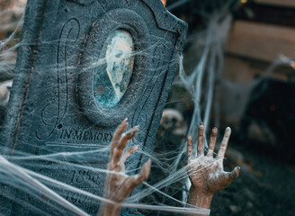 Poster - Muddy hands covered with cobweb coming out of the grave of a man - creepy Halloween background