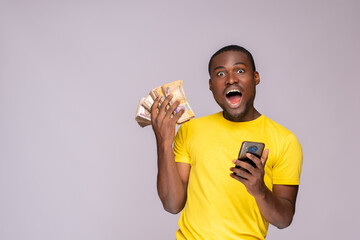 Wall Mural - happy and excited young nigerian man holding bundles of cash and phone