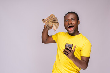 Wall Mural - happy and excited young african man holding bundles of cash and phone