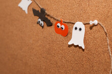 Homemade Paper Garland For Halloween In The Form Of Pumpkins, Ghosts And Bats With Eyes On A Jute Rope Close-up On A Blurred Background Of A Cork Board