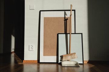 Stylish wooden broom and scoop standing in front of empty picture frames in new appartment. Cleaning concept.