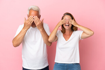 Wall Mural - Middle age couple isolated on pink background covering eyes by hands