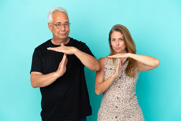 Wall Mural - Middle age couple isolated on blue background making stop gesture with her hand to stop an act