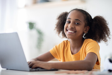 Cheerful black girl studying online, using laptop, typing on keyboard