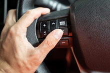 Action Of A Car Driver Is Pressing Button On Multifunction Wheel To Control Audio And Communication System. Transportation Technology Photo, Close-up And Selective Focus On The Thumb Finger.