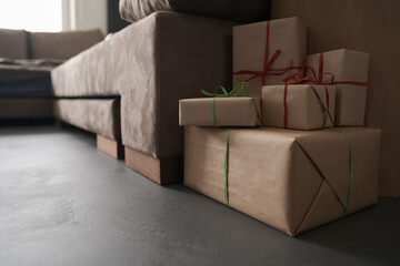 Wall Mural - presents in paper wrap with ribbons under christmas tree indoor near couch with warm light