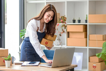 Beautiful young Asian business owner woman prepare parcel box and check online orders of product for deliver to customer. Shopping Online concept.