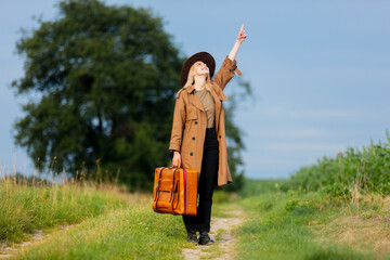 Sticker - Blonde woman in cloak and hat with suitcase walking on countryside road in village