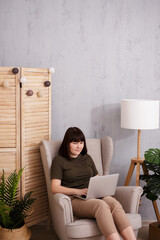 Wall Mural - portrait of woman sitting in armchair and using laptop with copy space