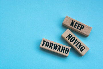 There is a blue notebook on a light blue background. Above are three wooden blocks with the words KEEP MOVING FORWARD