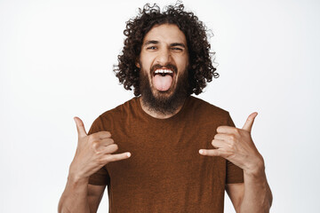 Wall Mural - Portrait of carefree middle eastern man showing tongue and yolo gesture, having fun, enjoying party, looking cool and happy, white background