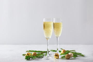 Glasses with sparkling wine type champagne with fir branches and golden Christmas tree decorations on light background