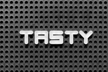 Sticker - White alphabet letter in word tasty on black pegboard background