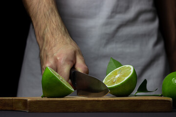 Poster - The chef cuts the lime on a wooden board. Sour fruit. Citrus fruit