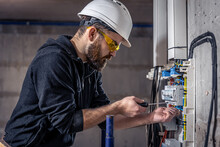 A Male Electrician Works In A Switchboard With An Electrical Connecting Cable.
