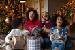 © fizkes - Excited young biracial family with two little children sit on floor near fir-tree have fun unpacking Christmas gifts. Happy African American parents and little kids enjoy New Year celebration at home.