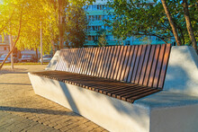 A Modern Concrete Bench Covered With Brown Wooden Slats In A City Park.