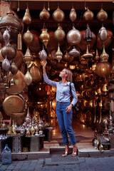 Wall Mural - Travel and shopping. Young traveling woman with choose presents in copper souvenir handicraft shop in Morocco.