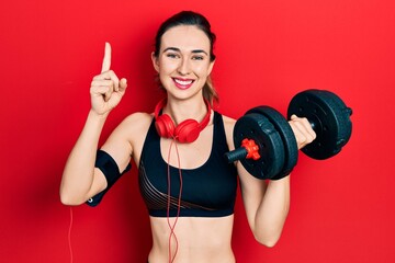 Poster - Young hispanic girl wearing sportswear using dumbbells smiling with an idea or question pointing finger with happy face, number one