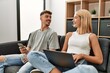 © Krakenimages.com - Young caucasian couple smiling happy using laptop and smartphone sitting on the sofa at home.
