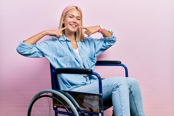 Poster - Beautiful blonde woman sitting on wheelchair smiling cheerful showing and pointing with fingers teeth and mouth. dental health concept.